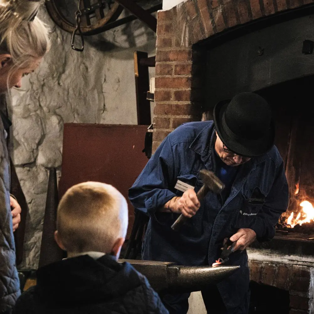 A blacksmith works in front of museum guests.