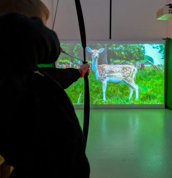 En ung dreng skyder med bue og pil i udstillingen STORT på Det Grønne Museum